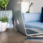 A contemporary home office setup featuring a sleek laptop, smartphone, and potted plants on a wooden table.