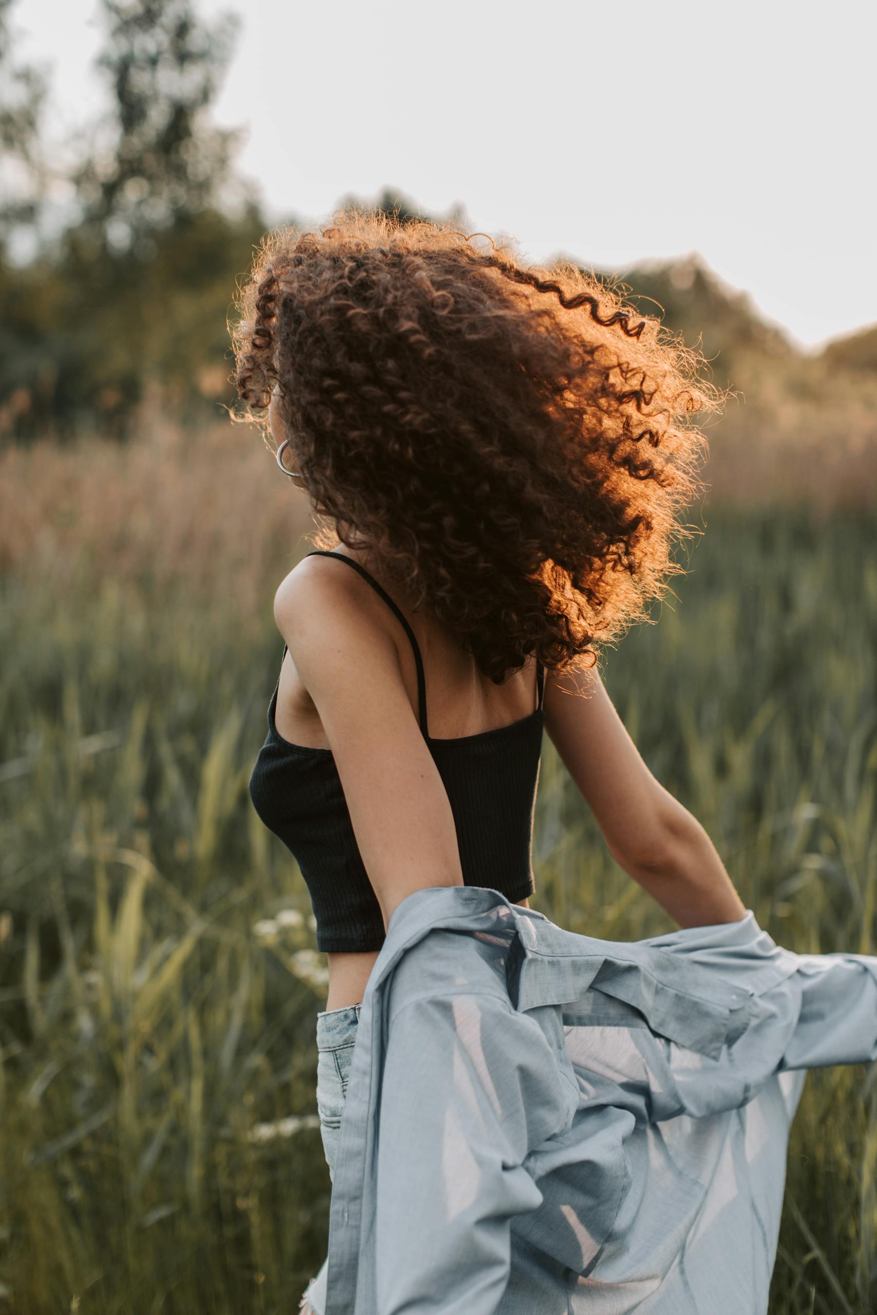 A woman with curly hair and a stylish outfit enjoys a carefree moment outdoors.