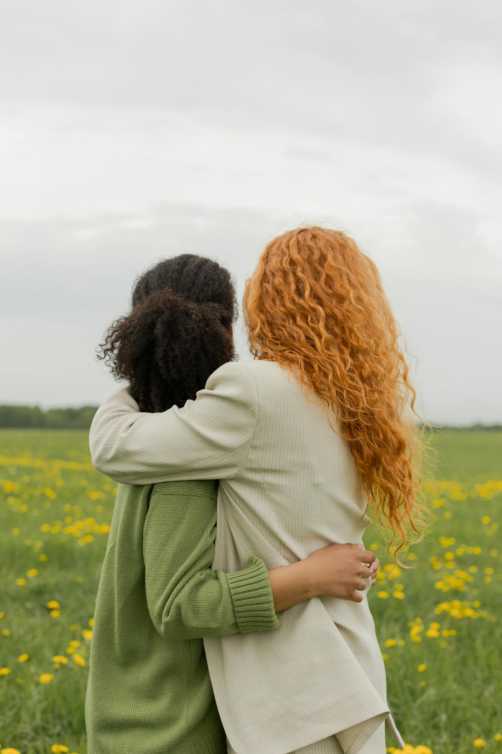 Two friends share an embrace in a vibrant summer meadow, surrounded by blooming flowers, expressing warmth and companionship.