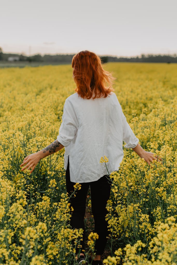 Woman with red hair walks in a yellow flower field, enjoying spring scenery.